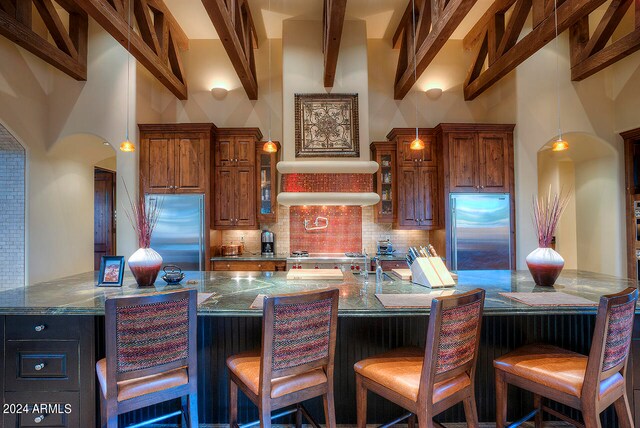 kitchen featuring a breakfast bar area, decorative backsplash, dark stone countertops, and stainless steel built in refrigerator