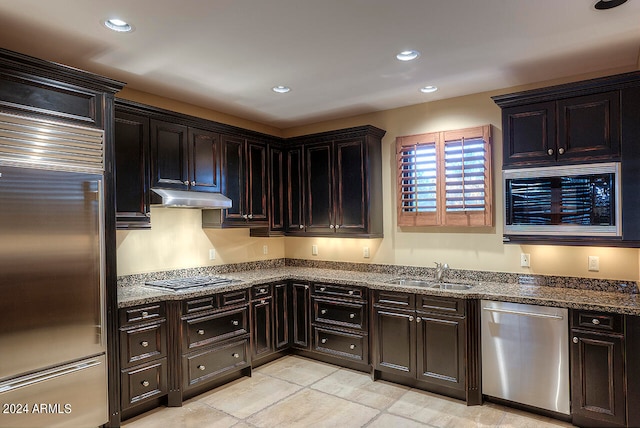 kitchen featuring appliances with stainless steel finishes, sink, stone countertops, light tile patterned flooring, and dark brown cabinets