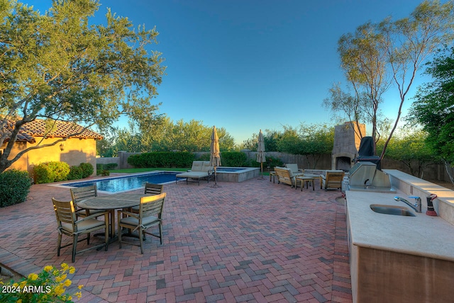 view of patio featuring a fenced in pool, exterior kitchen, sink, and exterior fireplace