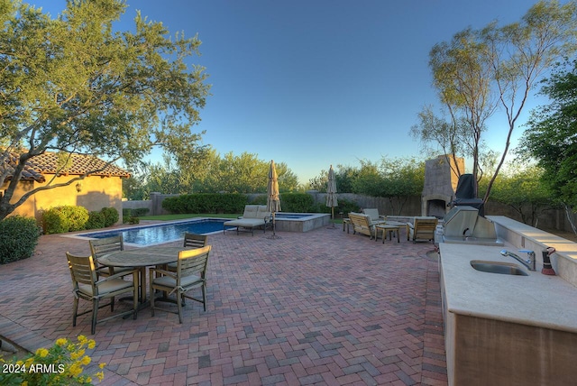 view of patio / terrace featuring area for grilling, sink, a fenced in pool, and an outdoor fireplace