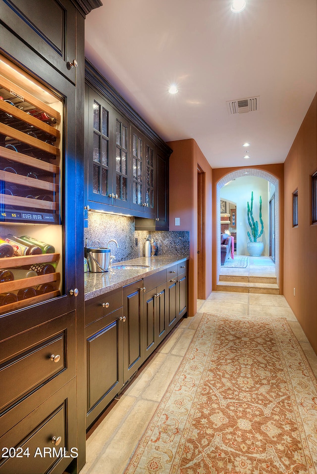 bar featuring decorative backsplash, sink, dark brown cabinetry, and light stone countertops