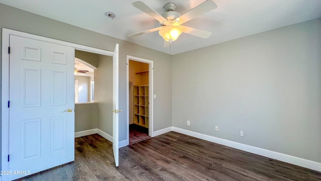 unfurnished bedroom featuring ceiling fan, a spacious closet, and dark hardwood / wood-style flooring