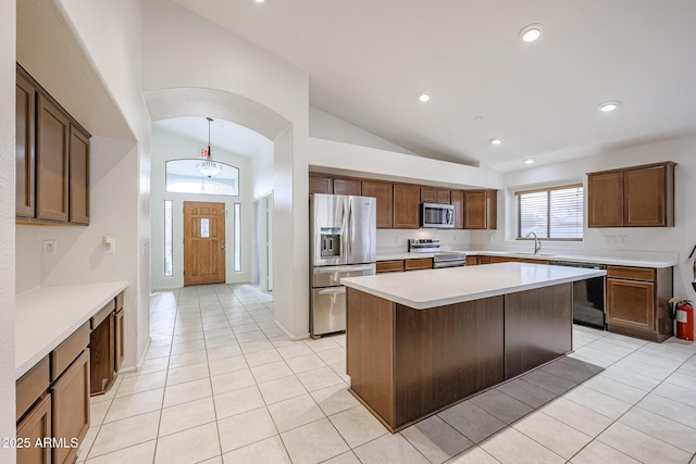 kitchen featuring appliances with stainless steel finishes, a kitchen island, sink, light tile patterned flooring, and high vaulted ceiling