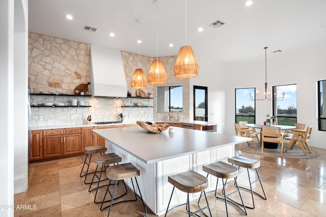 kitchen with a kitchen breakfast bar, backsplash, premium range hood, and decorative light fixtures