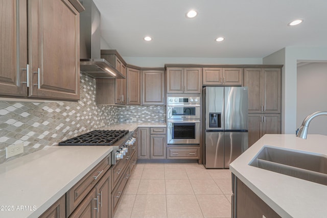 kitchen with sink, decorative backsplash, light tile patterned floors, stainless steel appliances, and wall chimney range hood