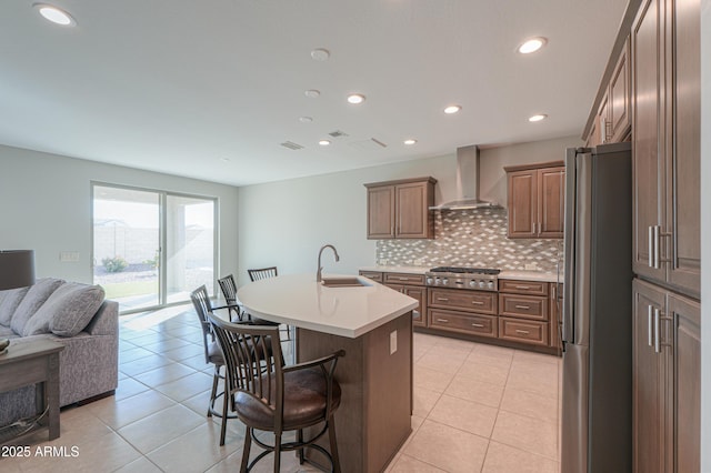 kitchen with appliances with stainless steel finishes, a breakfast bar, sink, wall chimney range hood, and a center island with sink