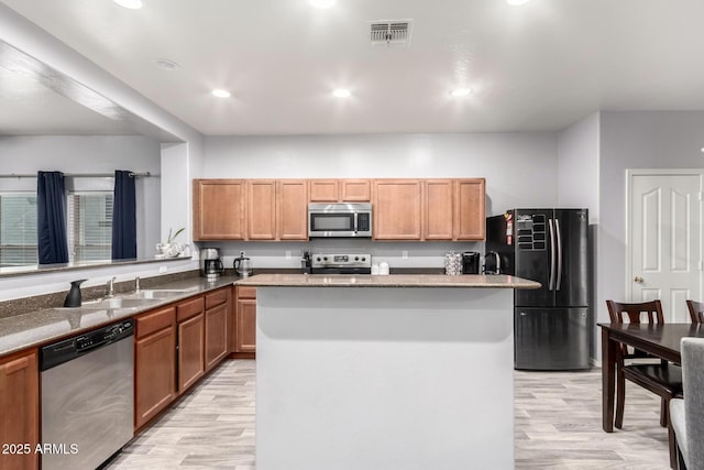 kitchen with stainless steel appliances, sink, a kitchen island, and light wood-type flooring