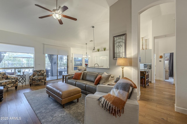 living room featuring wood-type flooring, ceiling fan with notable chandelier, and high vaulted ceiling