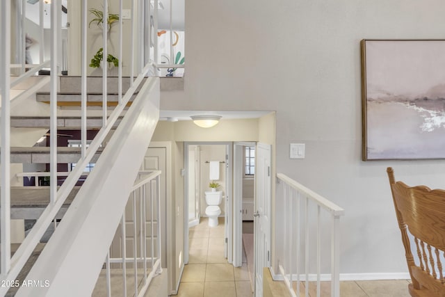 stairway featuring baseboards, a high ceiling, and tile patterned floors