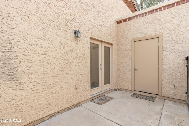 property entrance with a patio, french doors, and stucco siding