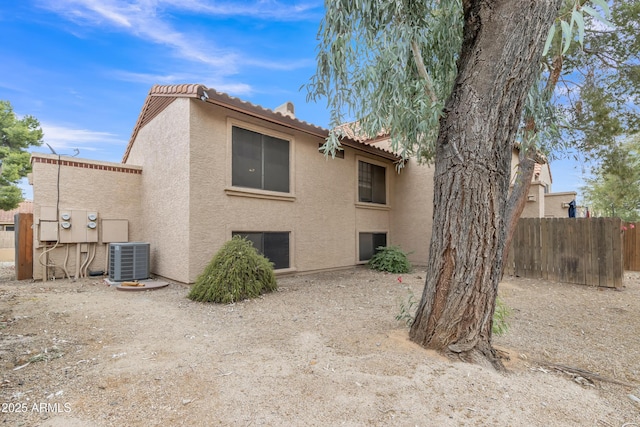 rear view of property featuring a tiled roof, central AC unit, fence, and stucco siding