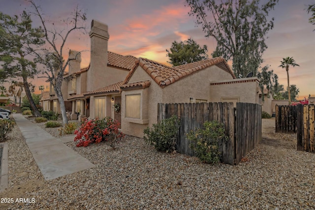 mediterranean / spanish house with a chimney, fence, a tiled roof, and stucco siding