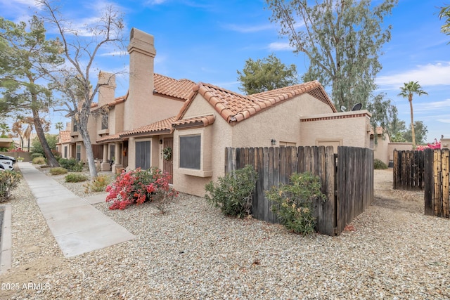 view of side of property with a tiled roof, a chimney, fence, and stucco siding