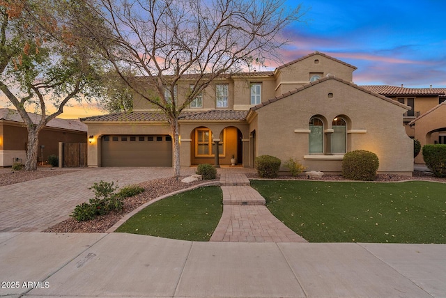 mediterranean / spanish-style house with a garage, decorative driveway, a tile roof, and stucco siding