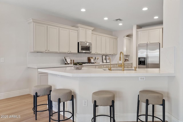 kitchen with visible vents, light wood-style flooring, a breakfast bar area, stainless steel appliances, and a sink