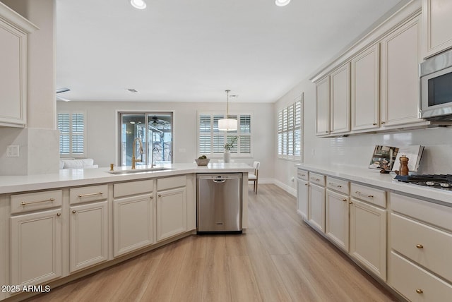 kitchen with light wood finished floors, stainless steel appliances, light countertops, a sink, and a peninsula