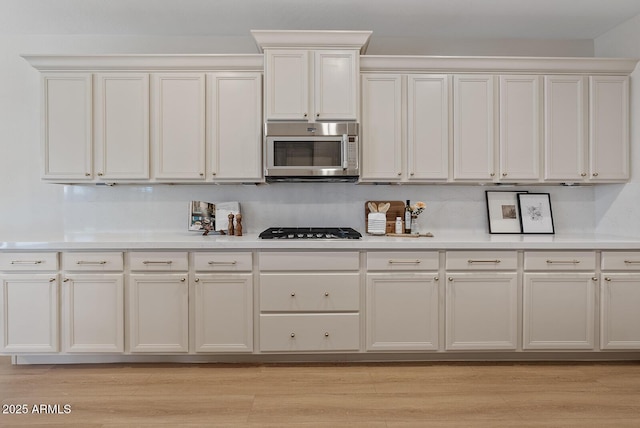 kitchen featuring black gas cooktop, light countertops, light wood finished floors, and stainless steel microwave