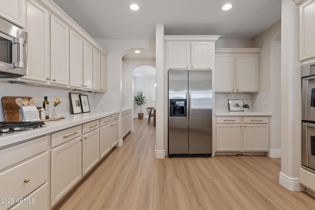 kitchen with arched walkways, recessed lighting, light countertops, appliances with stainless steel finishes, and light wood-type flooring