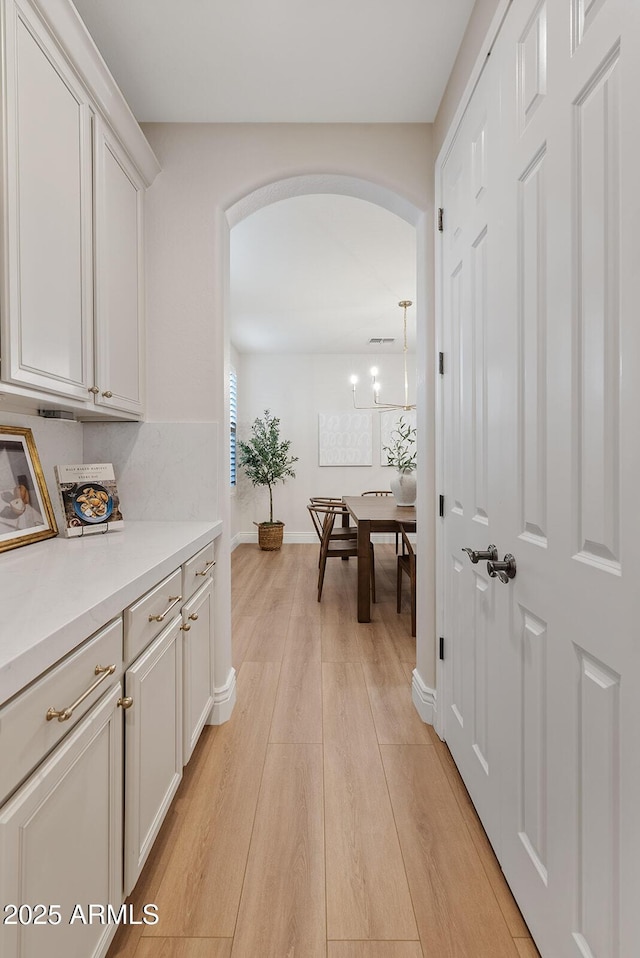 hall with arched walkways, visible vents, light wood-style flooring, and baseboards