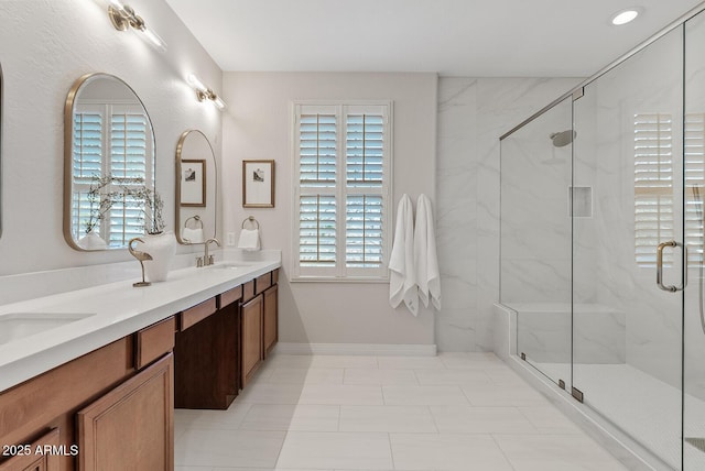 full bathroom featuring baseboards, a sink, a marble finish shower, and double vanity