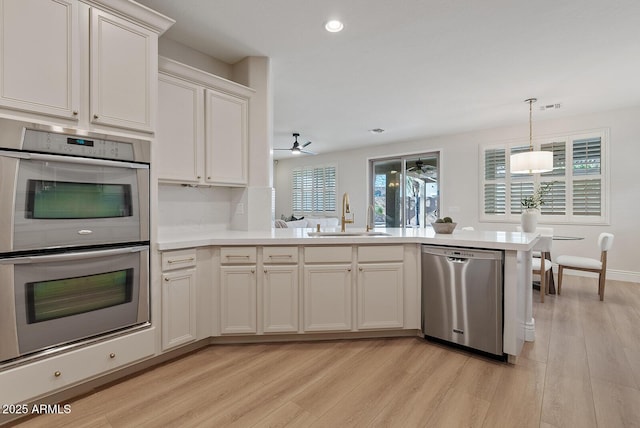 kitchen featuring light wood-style flooring, a peninsula, a sink, light countertops, and appliances with stainless steel finishes