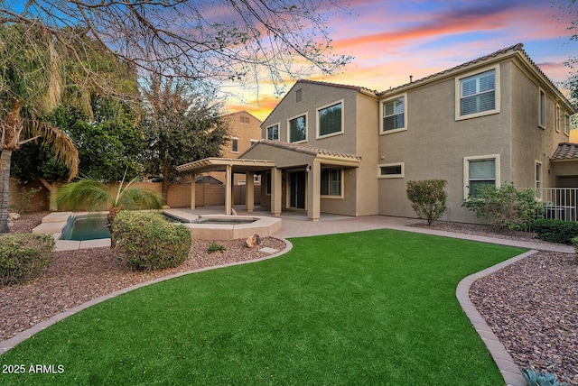 back of house at dusk featuring a patio, a fenced backyard, an in ground hot tub, a lawn, and stucco siding