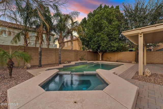 pool at dusk featuring a pool with connected hot tub, a fenced backyard, and a patio