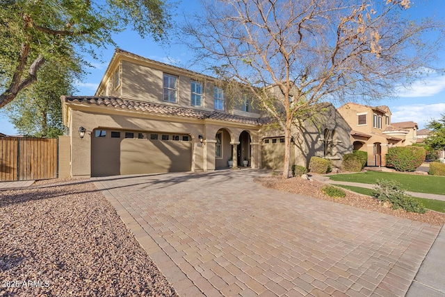 view of front of house featuring an attached garage, fence, a tile roof, decorative driveway, and stucco siding