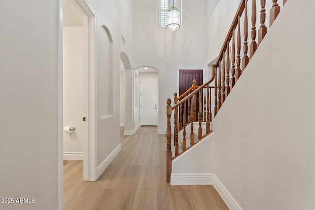 foyer entrance with arched walkways, baseboards, a towering ceiling, and light wood finished floors