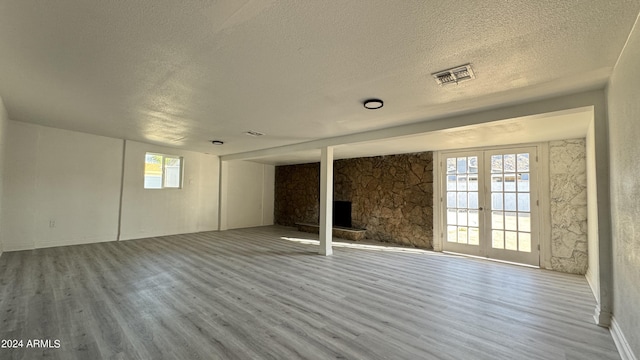 121 E Monte Way, Phoenix, AZ 85042 - unfurnished living room featuring wood finished floors, a textured ceiling, a stone fireplace, and french doors