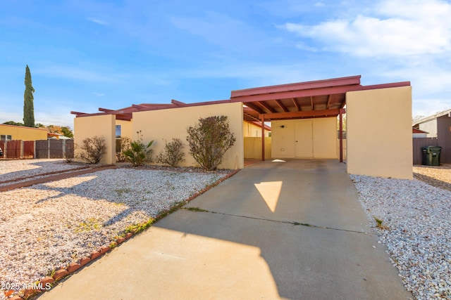 view of front of home featuring concrete driveway, fence, a carport, and stucco siding