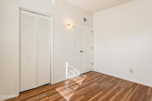 unfurnished bedroom featuring a closet, wood finished floors, visible vents, and baseboards