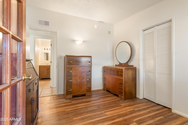 bedroom with a textured ceiling, a closet, wood finished floors, and visible vents