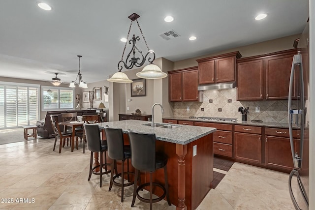 kitchen with ceiling fan, sink, light stone countertops, decorative light fixtures, and a kitchen island with sink