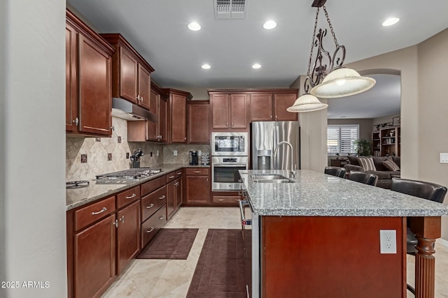 kitchen with a kitchen breakfast bar, stainless steel appliances, sink, hanging light fixtures, and an island with sink