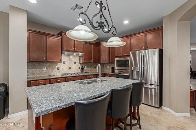 kitchen with sink, hanging light fixtures, stainless steel appliances, tasteful backsplash, and an island with sink