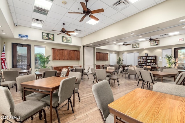 dining room featuring plenty of natural light, a drop ceiling, a high ceiling, and light wood-type flooring