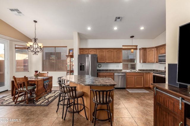 kitchen with sink, hanging light fixtures, stainless steel appliances, a kitchen island, and vaulted ceiling