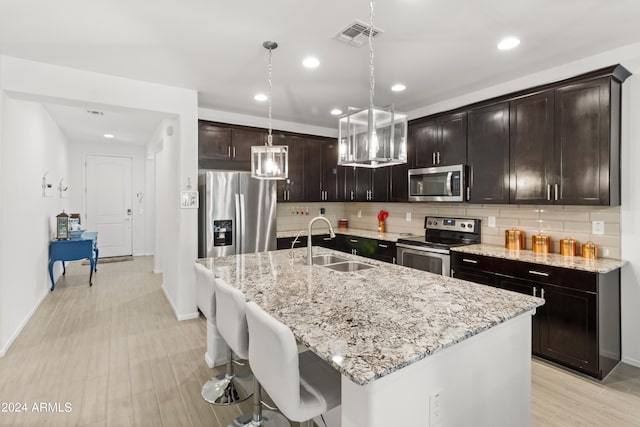 kitchen featuring light wood-type flooring, a sink, light stone counters, stainless steel appliances, and decorative backsplash