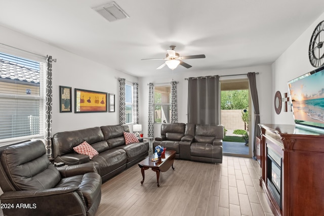 living room featuring ceiling fan, visible vents, light wood-style floors, and a glass covered fireplace