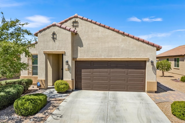 mediterranean / spanish house featuring a tiled roof, stucco siding, an attached garage, and concrete driveway