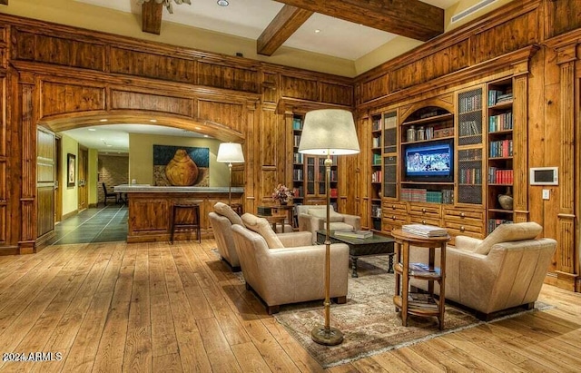 living room with beam ceiling, built in shelves, wooden walls, and hardwood / wood-style floors