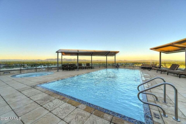 pool at dusk with a patio area and a community hot tub