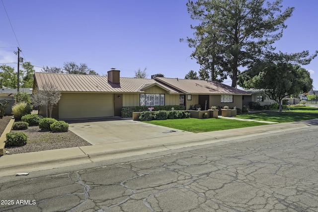 view of front facade featuring metal roof, a garage, driveway, a chimney, and a front yard