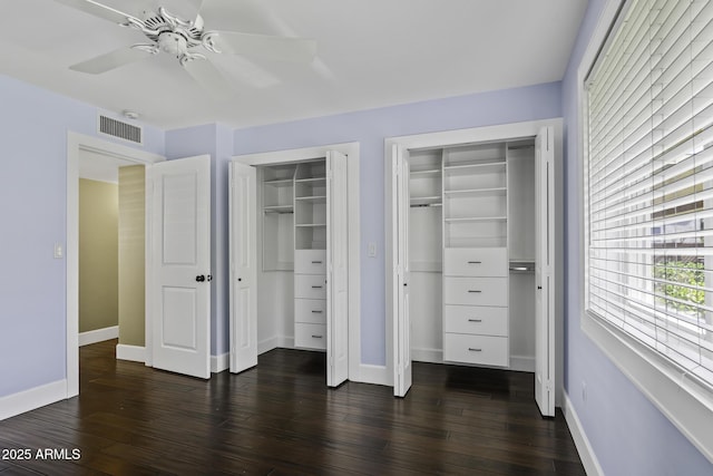 unfurnished bedroom with baseboards, visible vents, a ceiling fan, dark wood finished floors, and multiple closets