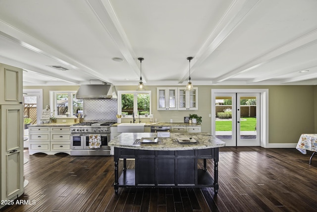 kitchen featuring beam ceiling, dark wood finished floors, stainless steel appliances, a sink, and wall chimney exhaust hood