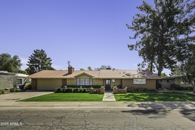 ranch-style house featuring an attached garage, metal roof, concrete driveway, and a front yard