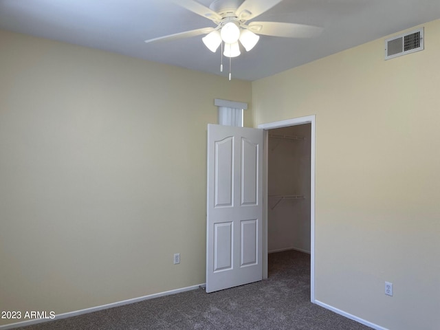 unfurnished bedroom with a closet, a spacious closet, dark colored carpet, and ceiling fan