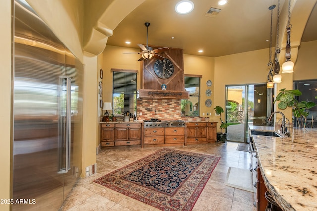 kitchen featuring visible vents, brown cabinetry, ceiling fan, arched walkways, and a sink