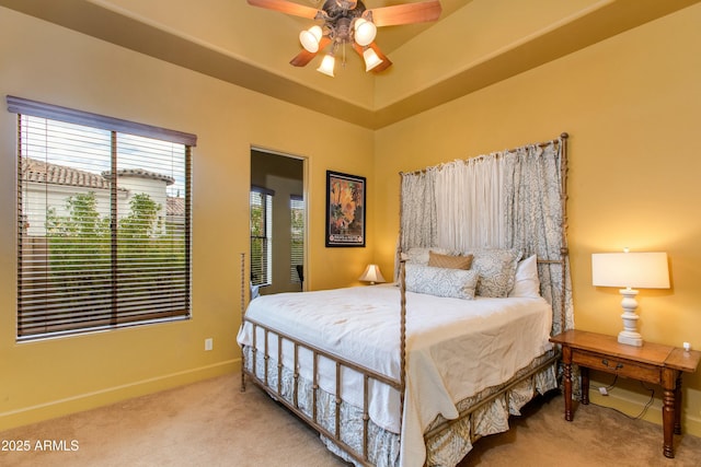 carpeted bedroom featuring a raised ceiling, a ceiling fan, and baseboards